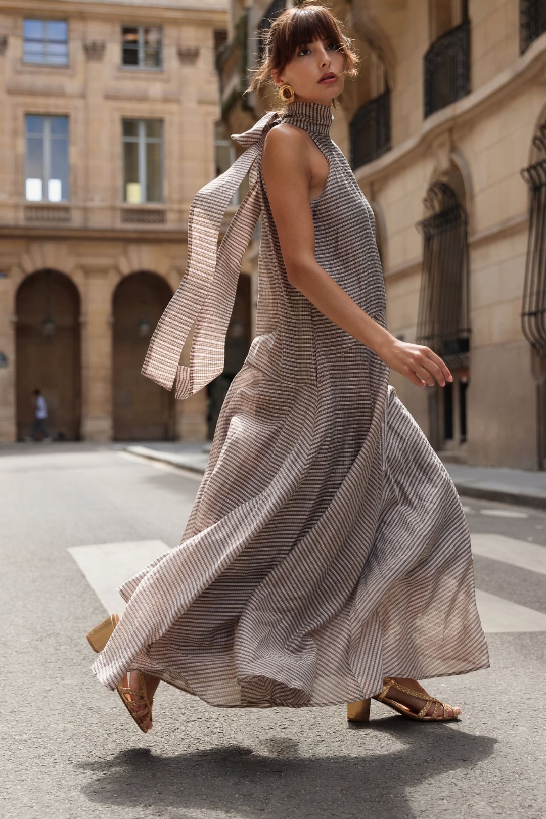 Model walking in the Zandra Stone Victoria Scarf Dress - Brown Plaid on a European city street.